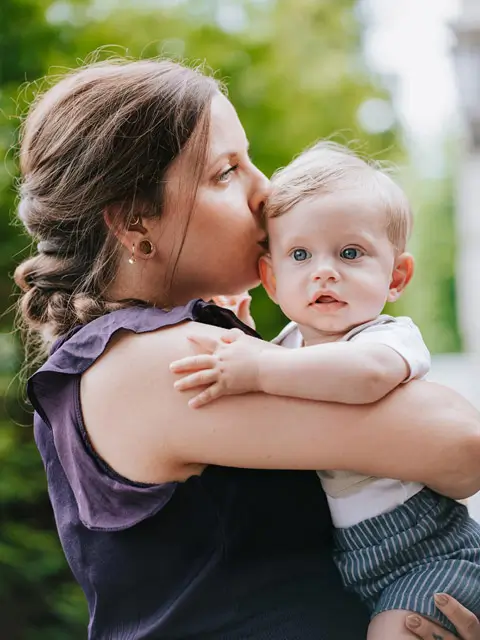 Kinderwillkommensfest 4 Mutter hält liebevoll ein hellblondes Baby im Arm und küsst es